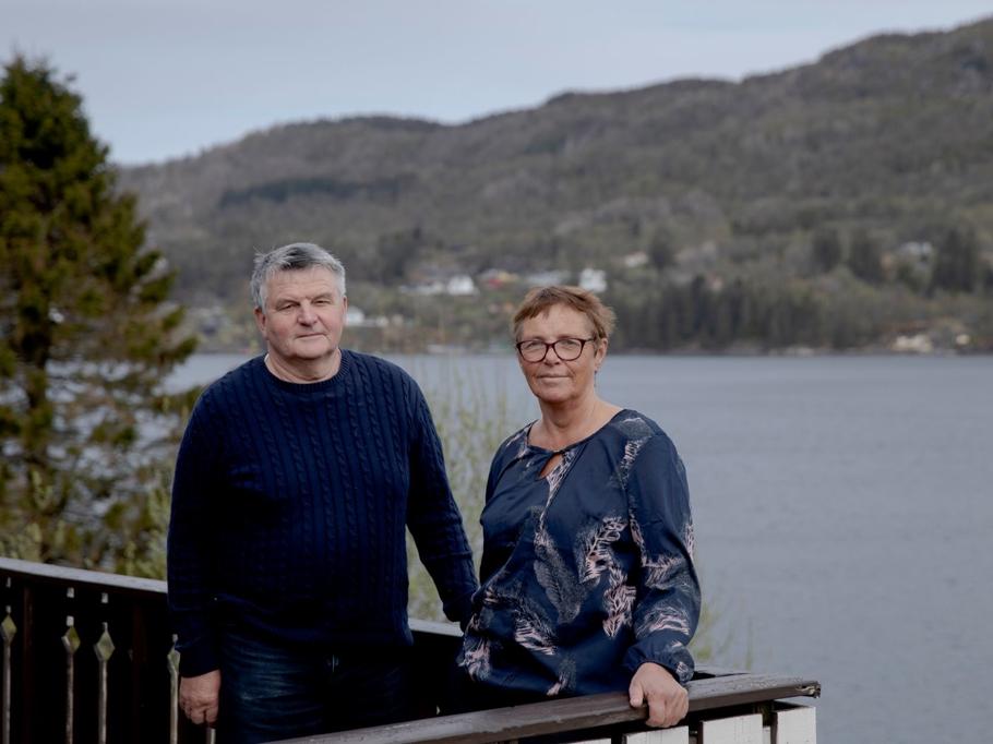 Mann og kvinne står på altan med fjord og fjell i bakgrunnen