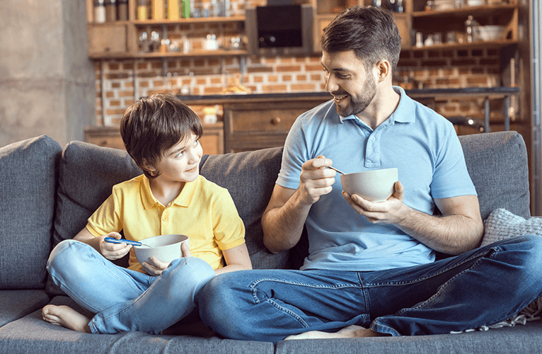 far og sønn sitter i sofaen og spiser mat