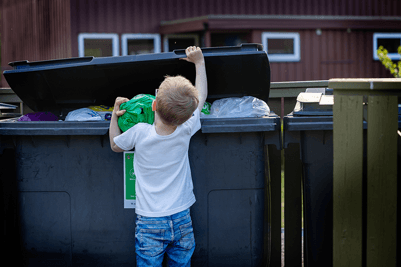 Barn kaster søppelpose i søppelkasse.