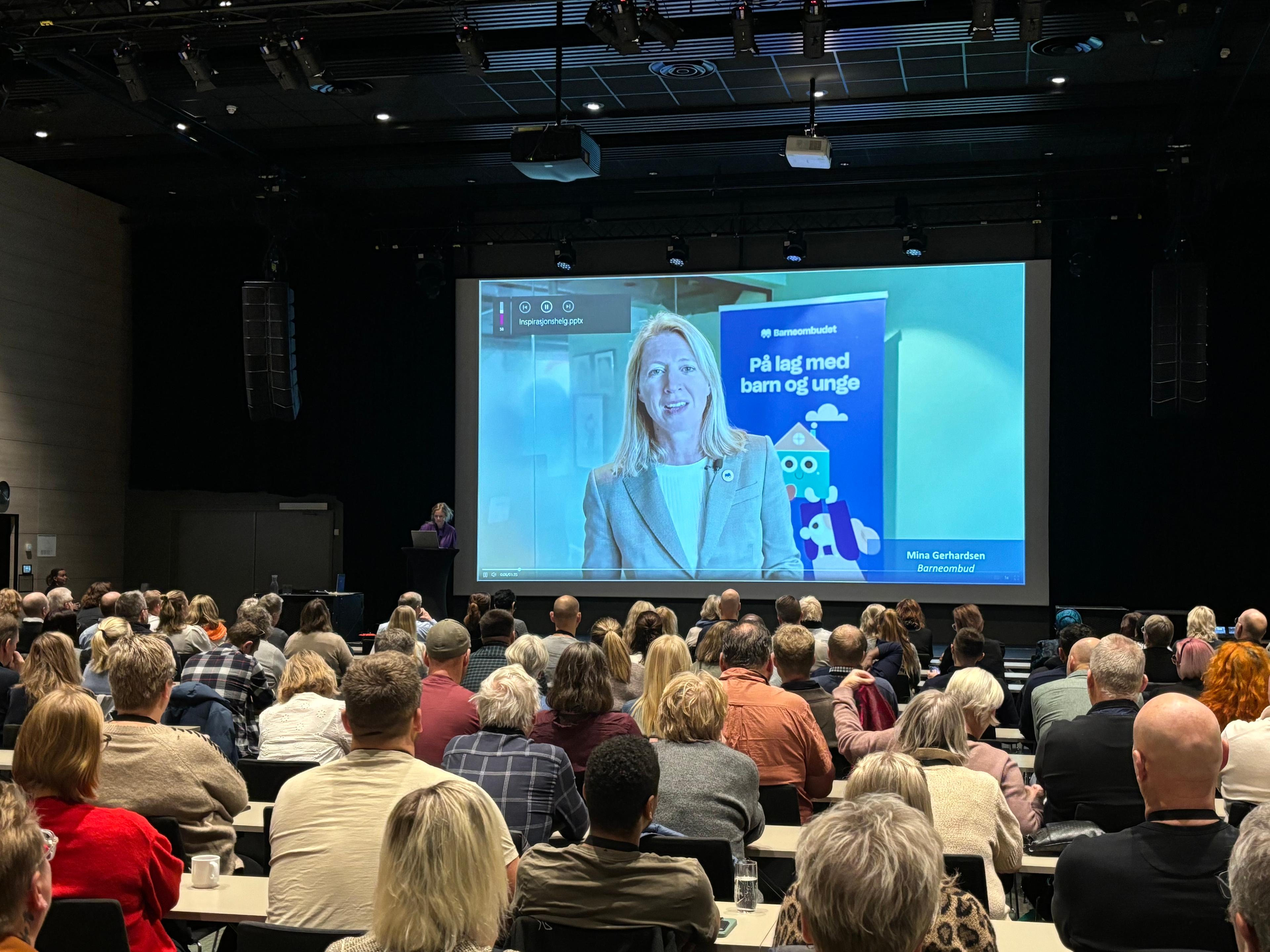 Mange personer sitter i salen og hører på presentasjon på skjerm