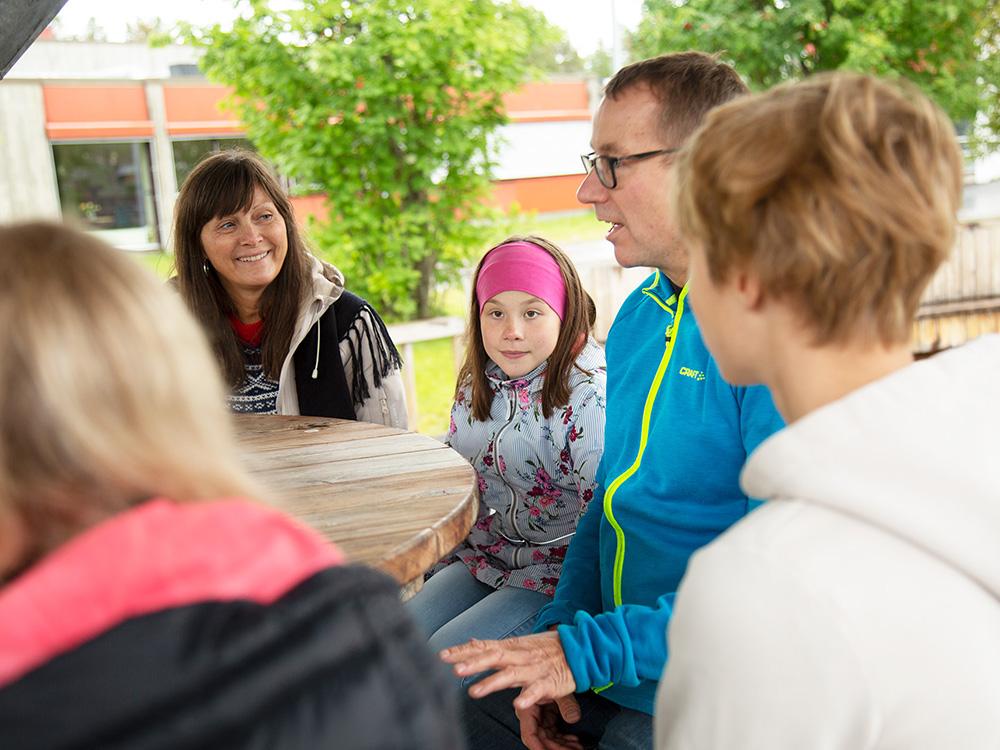 En familie med to voksne, et barn og to ungdommer sitter utendørs