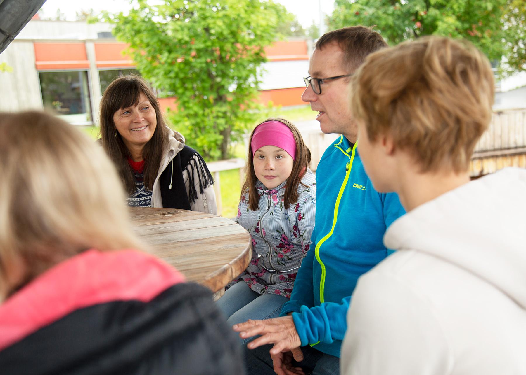 En familie med to voksne, et barn og to ungdommer sitter utendørs