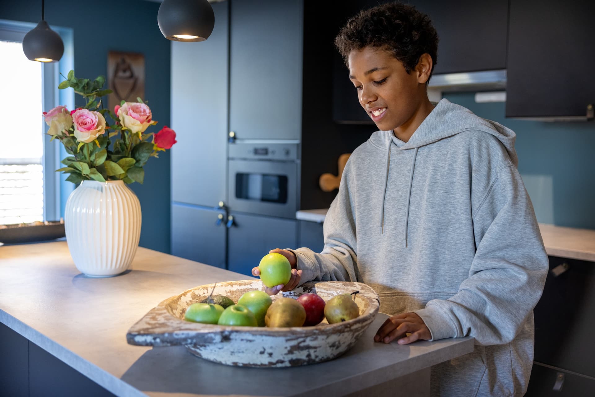 Ung person står på kjøkkenet og holder et eple ved en fruktskål