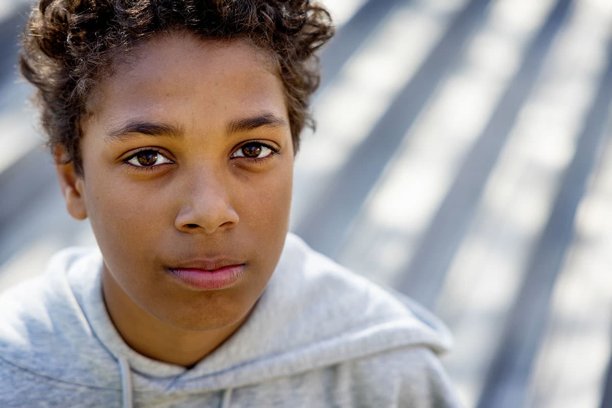 Ung person med alvorlig uttrykk ser i kameraet utendørs