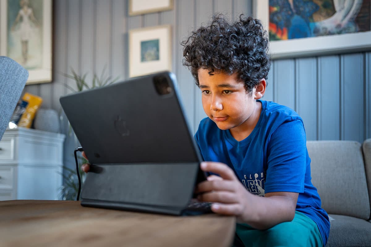 Et barn sitter i sofaen og ser på et nettbrett