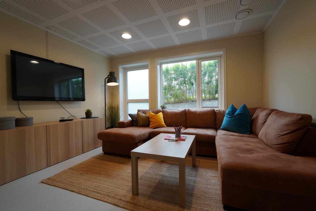 En stue med brun hjørnesofa og tv på veggen.