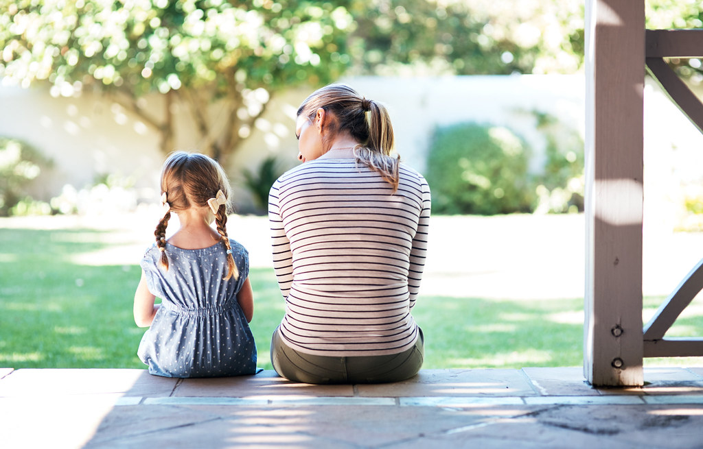 En voksen og et barn sitter ute på en veranda. 